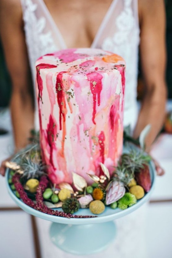 a bright watercolor wedding cake with drip and gold leaf surrounded by greenery and blooms is a lovely idea to try