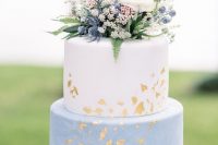 52 a catchy spring or summer two-tier wedding cake with a white and watercolor blue tier, some greenery, thistles, berries and a bloom on top