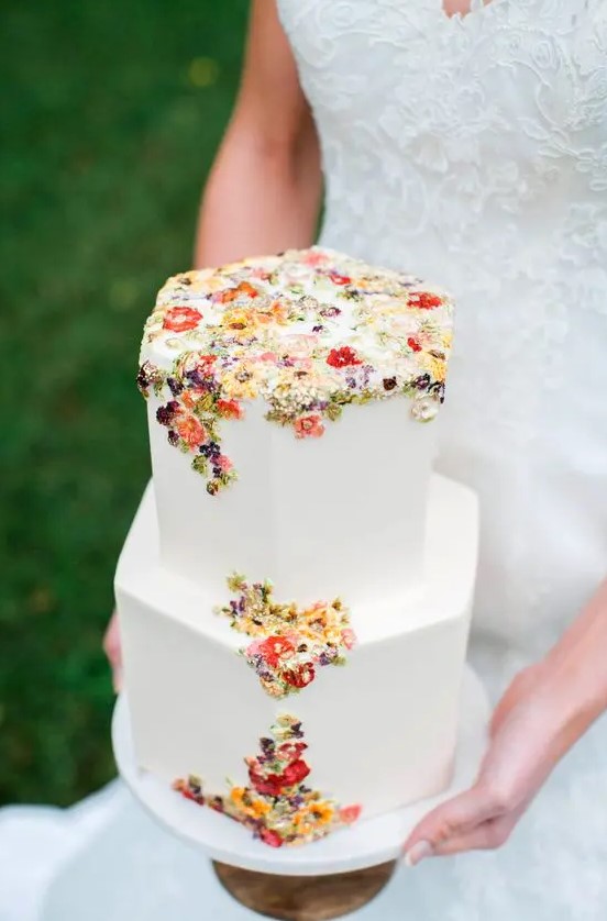 a chic hexagon white wedding cake with colorful sugar and pressed blooms and foliage is a gorgeous idea for a secret garden wedding