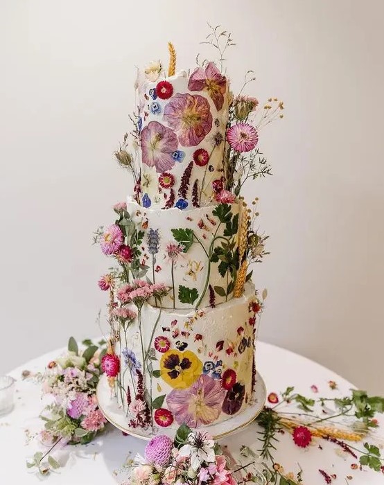 a fantastic wedding cake covered with white buttercream and with bright dried flowers and leaves pressed to it and attached for a voluminous look