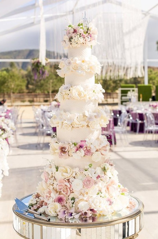 a glam wedding cake with white patterned tiers, white and blush blooms, very lush and chic
