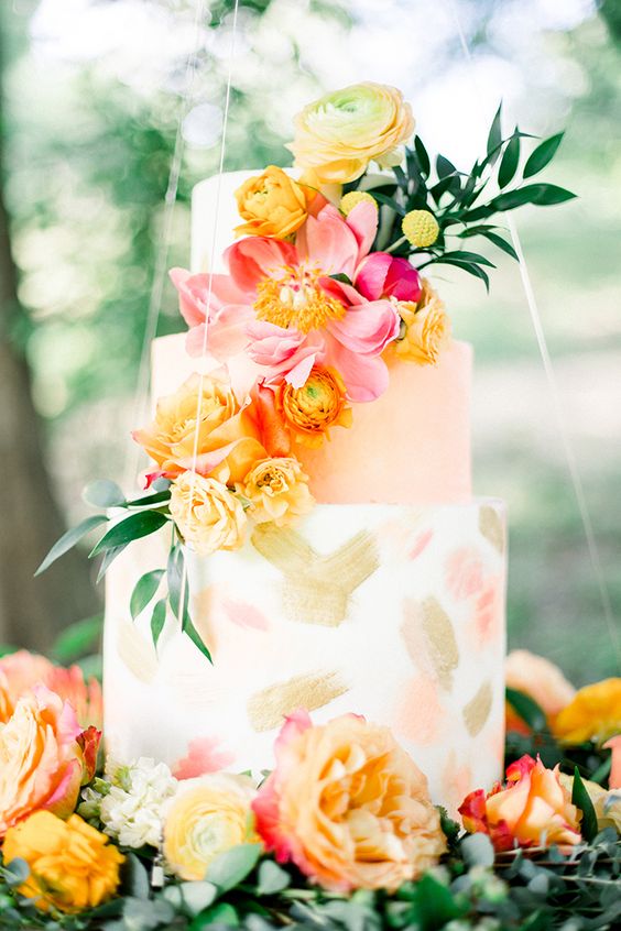 a gorgeous summer wedding cake with white and peachy tiers, with gold and croal brushstrokes, with yellow and pink blooms and a greenery branch is a fantastic statement