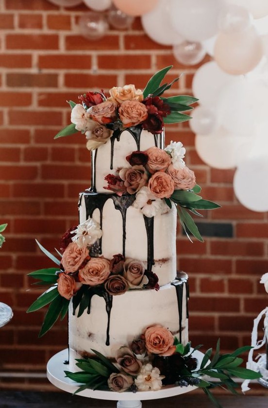 a jaw-dropping three-tier wedding cake with chocolate drip, mauve and peachy blooms, greenery is a chic idea for any wedding