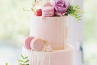 69 a light pink wedding cake with creamy drip, gold foil, bright blooms and greenery, pink macarons and a gold calligraphy topper