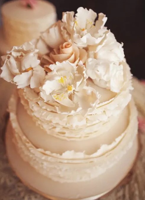 a neutral buttercream wedding cake with ruffles and sugar blooms on top is a gorgeous idea for a spring or summer wedding