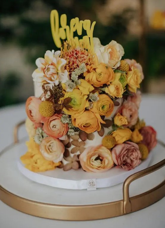 a unique one tier wedding cake with pink, rust, yellow and mustard blooms, dried and fresh, a yellow topper