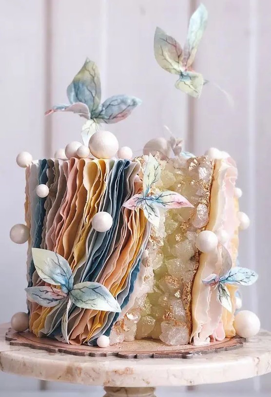 a unique wedding cake with a geode touch, layered pastel ruffles, mini snowballs, pastel sugar blooms is a lovely idea