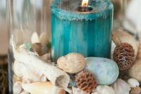 a beach wedding decoration of seashells, pinecones, driftwood, beach sand and a teal candle is bold and cool