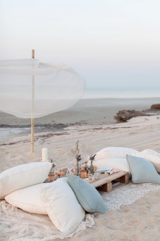 a beach wedding picnic table with lots of pillows, candles, dried blooms and air plants is amazing