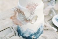a beautiful beach wedding cake with blue watercolors, corals and seashells is chic and elegant