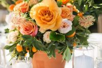 a beautiful summer wedding centerpiece of peachy, yellow and rust-colored blooms, foliage and kumquats