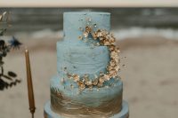a blue textural beach wedding cake with gold flowers and gold brushstrokes is a chic and romantic idea