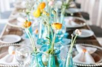 a bright and simple cluster wedding centerpiece of blue bottles and yellow blooms is lovely and stylish