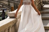 a jaw-dropping A-line wedding dress with a flowy pleated skirt with a train and a fantastic lace and rhinestone illusion back with cap sleeves