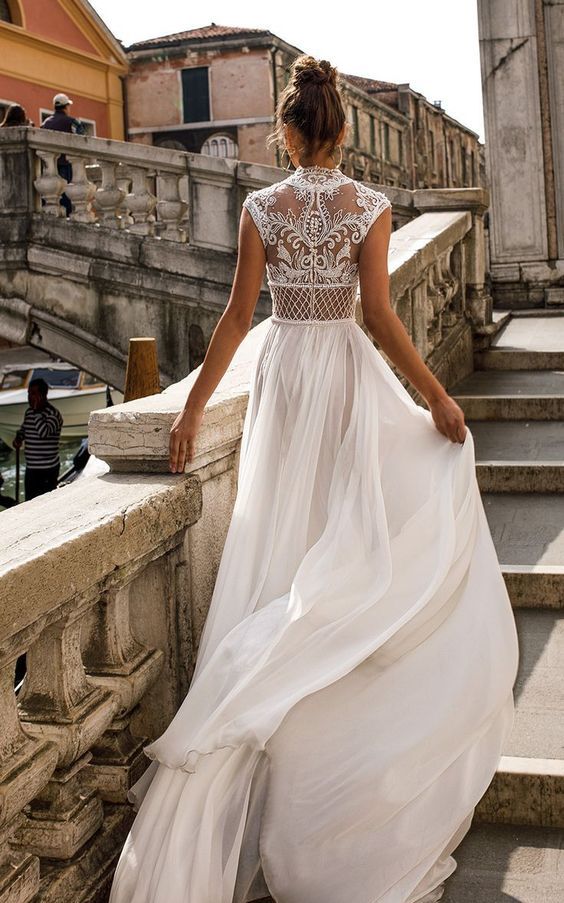 a jaw-dropping A-line wedding dress with a flowy pleated skirt with a train and a fantastic lace and rhinestone illusion back with cap sleeves