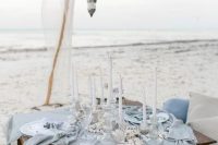 a light blue beach picnic tablescape with a lovely runner, candles, seashells and starfish, candle lanterns over the table