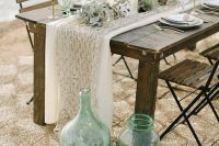 a lovely beach wedding tablescape with a net runner, air plants, herbs, candles and some jars, bottles and floats for decor
