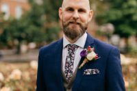 a navy suit, a tweed beige waistcoat, a florla tie and a matchiing handkerchief plus a floral boutonniere