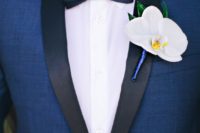 a navy tuxedo with black lapels, a black bow tie and a white orchid boutonniere for a refined tropical groom’s look