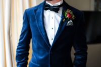 a navy velvet blazer, a white shirt with black buttons, a black bow tie and a bright floral boutonniere
