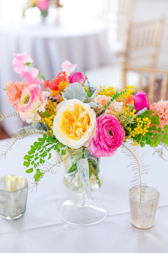 a super colorful summer wedding centerpiece of hot pink, peachy and red blooms, leaves and berries is chic