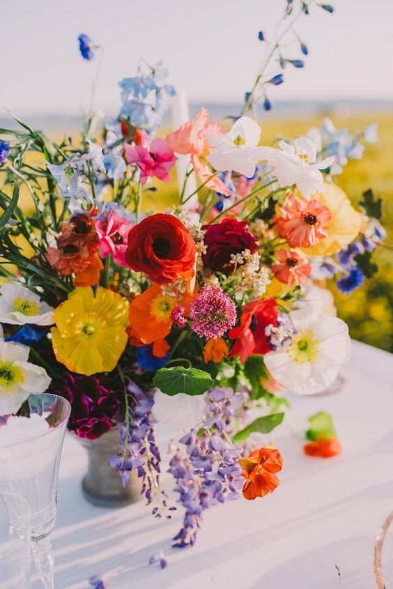 a super vibrant summer wedding centerpiece of red, yellow, purple, white, pink and rust blooms and greenery
