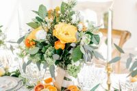 a vibrant summer wedding centerpiece of foliage, some white and yellow blooms and touches of orange