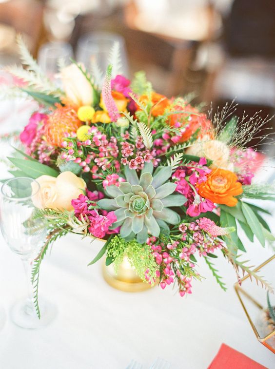a vibrant summer wedding centerpiece of pink, orange, yellow and fuchsia blooms, foliage and a statement succulent