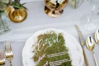 an acryclic and moss wedding menu with white calligraphy and printing is a great natural touch to the space