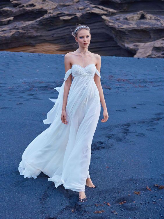 an off the shoulder flowy wedding dress with a draped embellished bodice and a flowy skirt