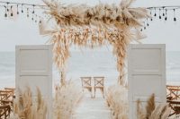 maximalist beach wedding decor with pampas grass, white blooms, simple chairs and white woven lamps