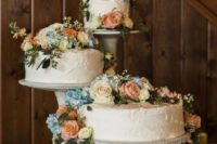 neutral wedding cake stands with blue, peach and white blooms and greenery on the table and cakes
