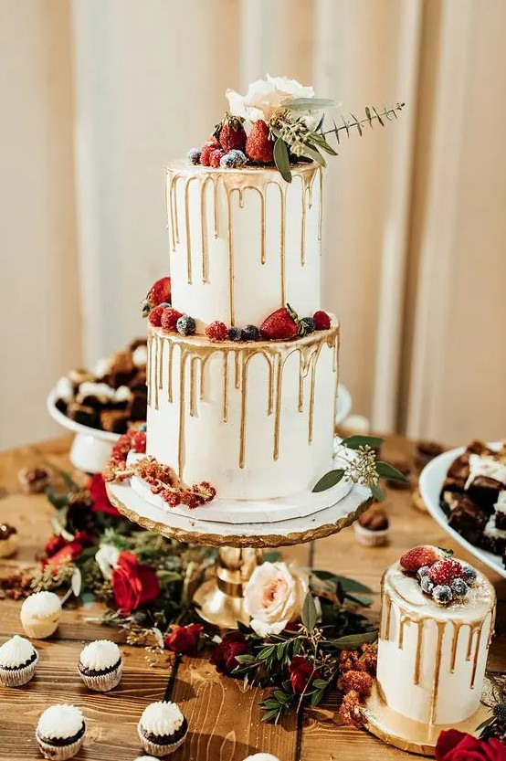 a Christmas wedding cake with gold drip, sugared berries, a white bloom and greenery is a very refined dessert