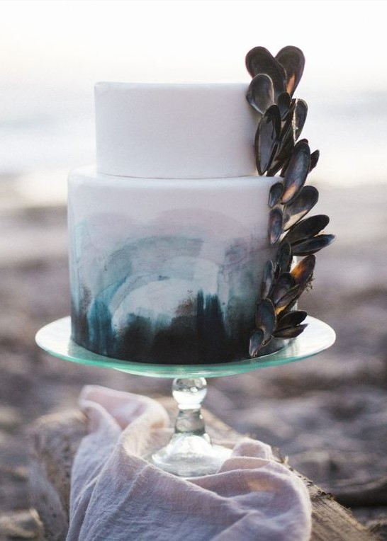 a beach wedding cake in white, with teal, grey and pink brushstrokes and mussel shells attached is wow