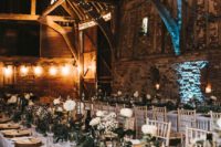 a beautiful barn wedding tablescape with a greenery and white rose runner, wood slice chargers and antlers