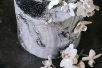 a beautiful black and white wedding cake with watercolors, silver glitter and white blooms on top looks ethereal