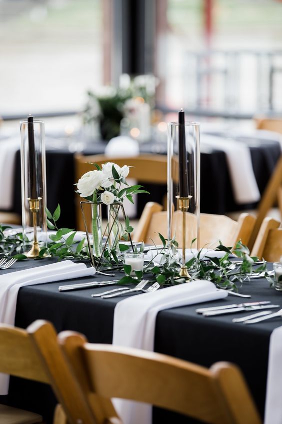 a beautiful monochromatic table setting with greenery, white blooms and black candles and white napkins