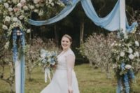 a beautiful wedding arch styled with lush blooms, greenery, pwoder blue fabric and branches