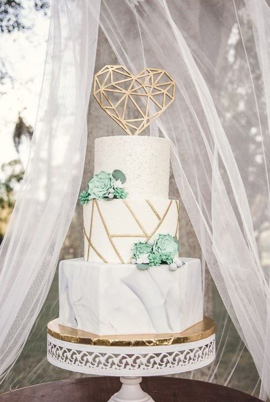 a beautiful wedding cake with a white marble, geometric and textural tier, with succulents and a gold geometric heart