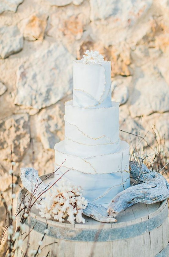 a beautiful white and watercolor blue wedding cake with a gold edge, a coral on top is amazing for a beach wedding
