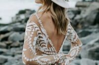 a boho bridal look with a nude and white lace applique wedding dress with long sleeves and a deep cutout back, a white hat with neutral blooms