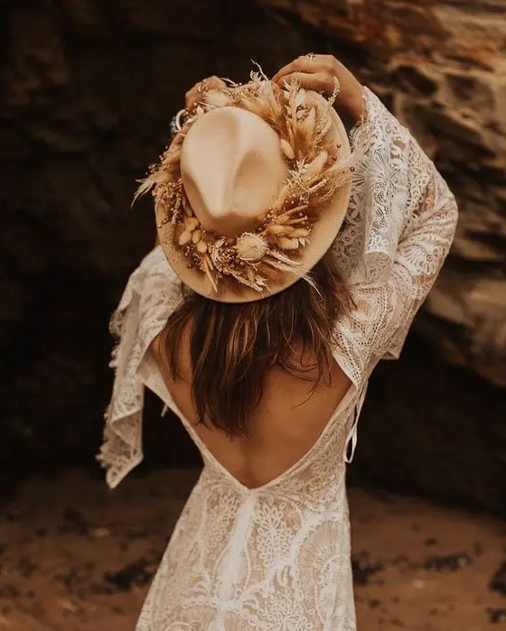 a boho bridal look with boho lace A-line wedding dress with a cutout back and bell sleeves, a tan hat with dried blooms and grass
