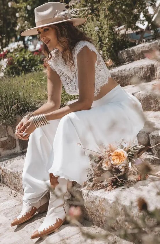 a boho western bridal look with a lace crop top, a plain midi skirt, cowboy boots and a neutral hat decorated with dried grass