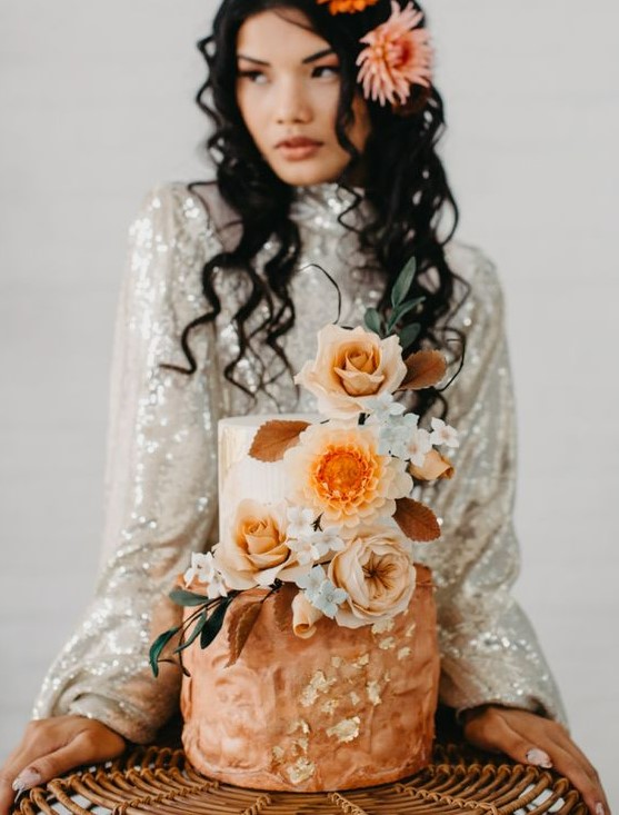 a bold and cool wedding cake with a blush and rust tier, with plenty of texture, pastel and bold blooms and gilded leaves for a 70s celebration