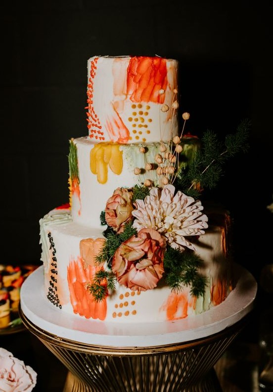 a bold color block wedding cake with orange, mustard, rust and green detailing, fresh blooms and berries and greenery