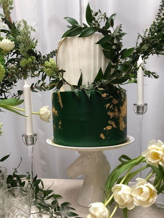 a bold emerald and white wedding cake with a pleated tier and a sleek one with gold leaf and a hoop with greenery for a modern wedding