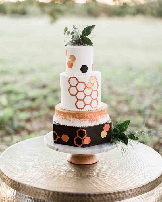 a bold white, black and copper wedding cake with watercolors and hexagons all over the cake plus greenery and blooms is a lovely idea