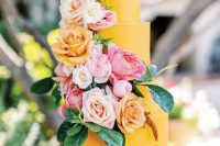 a bright yellow wedding cake with blush, peachy, pink and white blooms and leaves is a cool and fun idea to rock