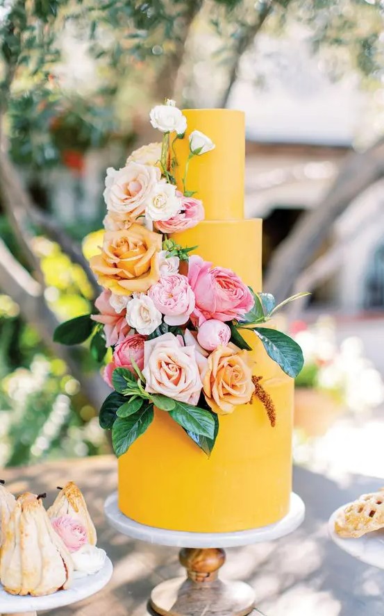 a bright yellow wedding cake with blush, peachy, pink and white blooms and leaves is a cool and fun idea to rock