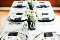 a casual monochromatic talescape with black chargers, napkins, vases and white blooms and all the rest in white